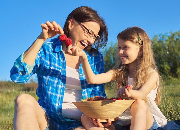 Happy laughing mother and child daughter together, picnic with bowl of fresh strawberries
