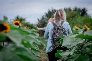 Mum walking down the sunflower field with child trying to grab the flowers
